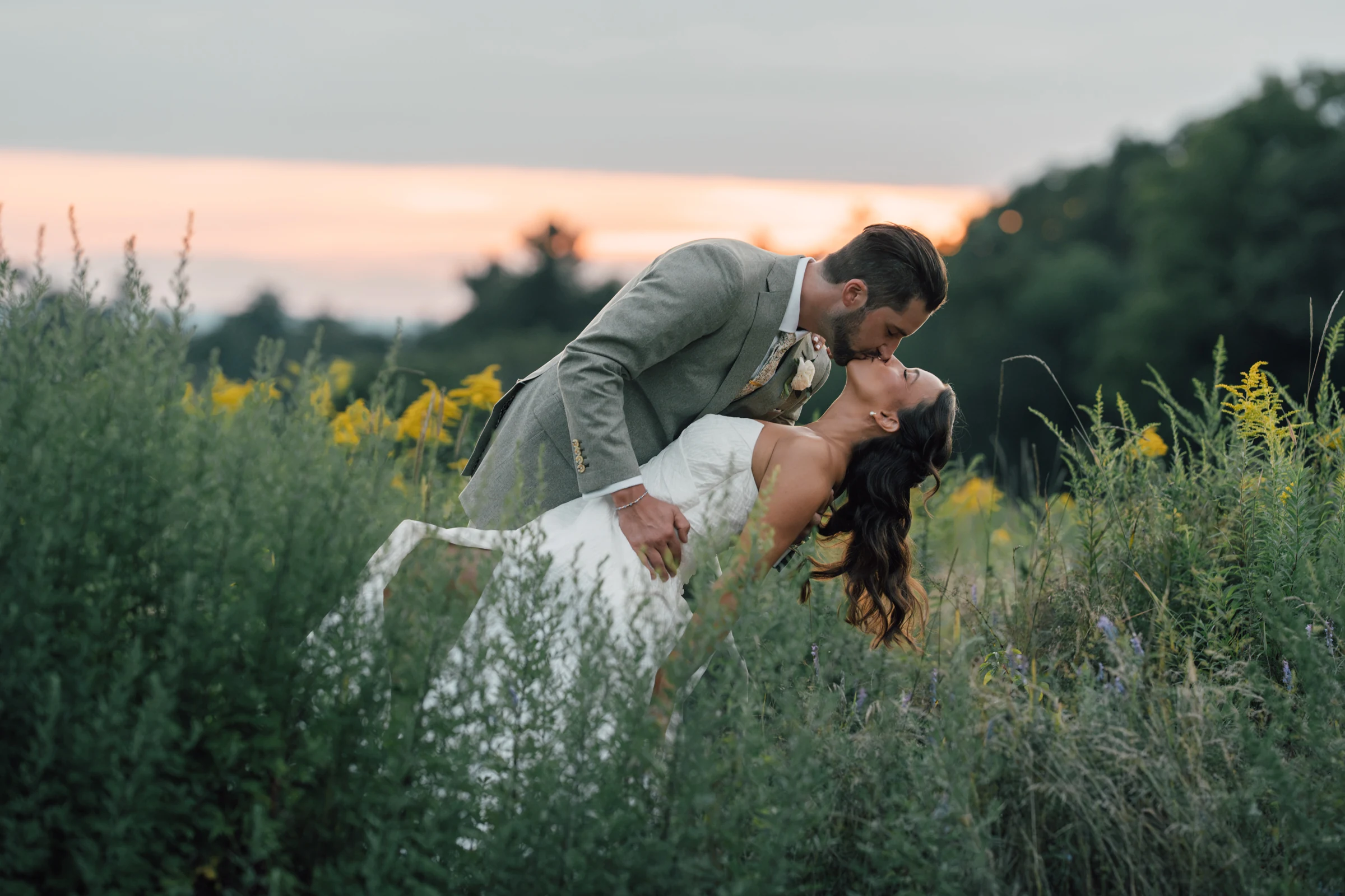 Newlyweds sharing a dip and kiss in a meadow at sunset at Harrington Farm, Princeton, Massachusetts