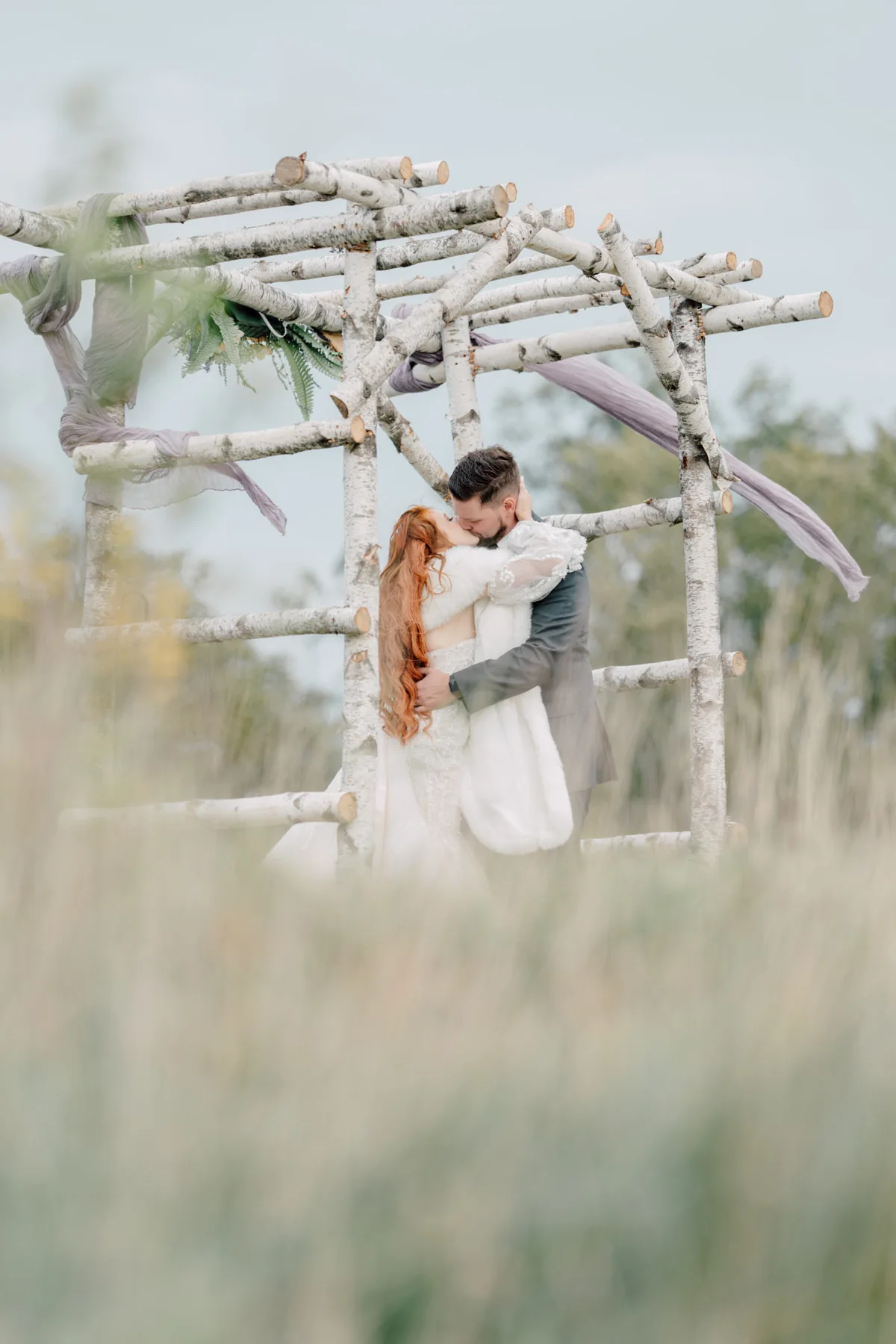 Newlyweds embracing beneath a driftwood wedding arch