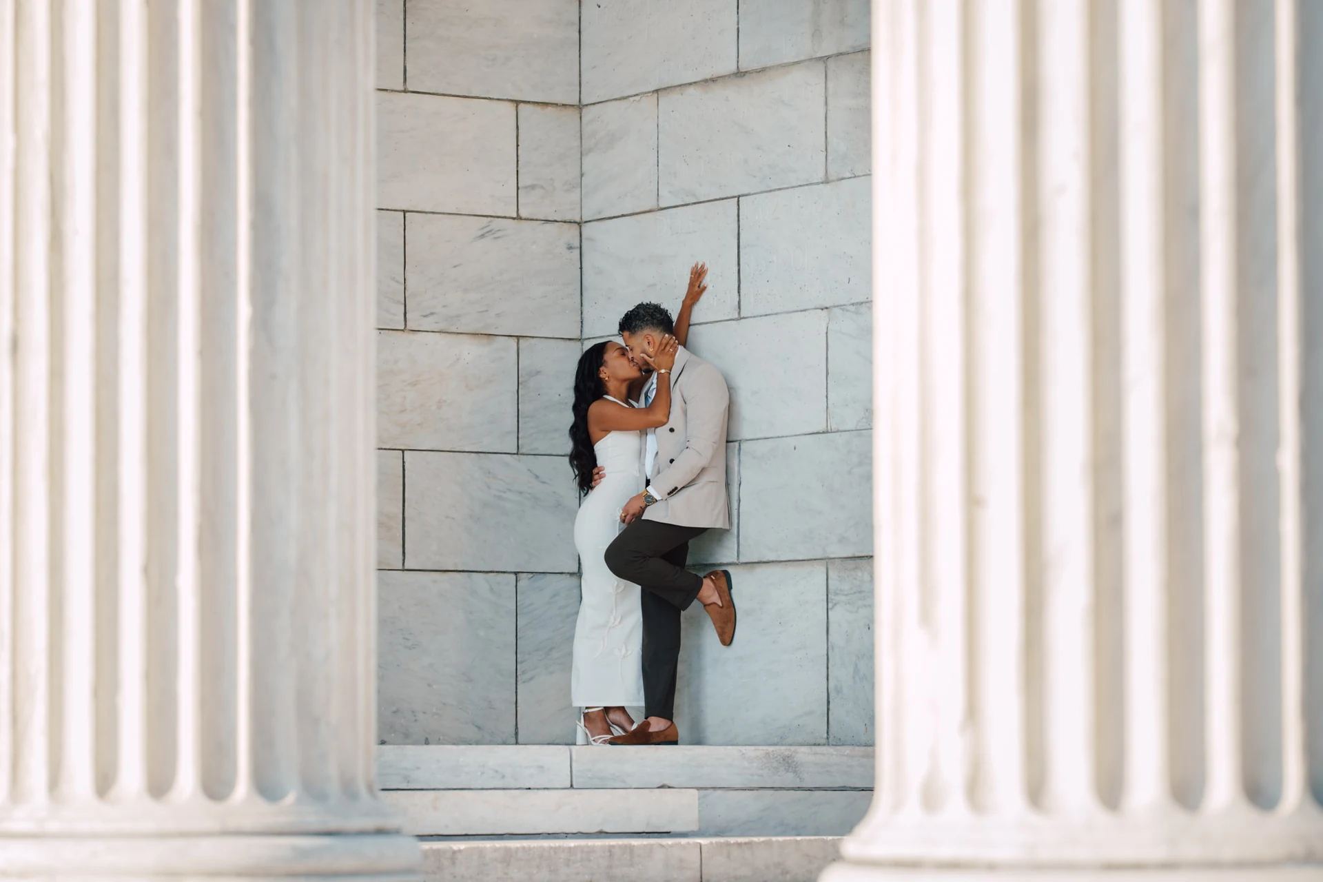 A bride and groom embracing between pale stone columns